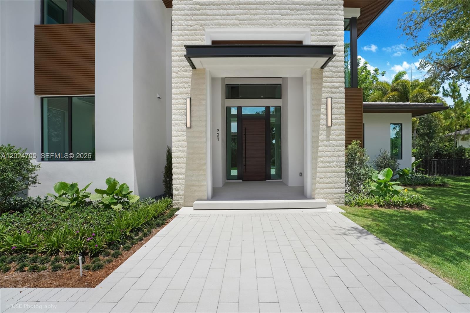 The exterior of a modern home features a stone facade, a wood door, and pavers — 9405 SW 72nd Ct, Pinecrest FL 33156, PINECREST, FL