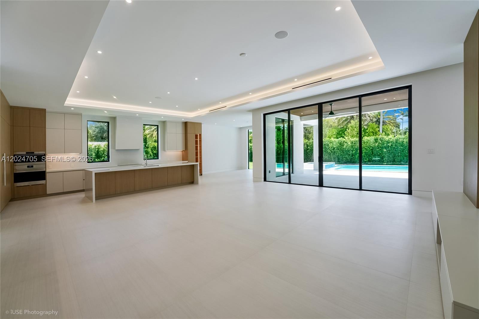 A modern open-concept kitchen and living area features light tile floors and large sliding glass doors — 9405 SW 72nd Ct, Pinecrest FL 33156, PINECREST, FL