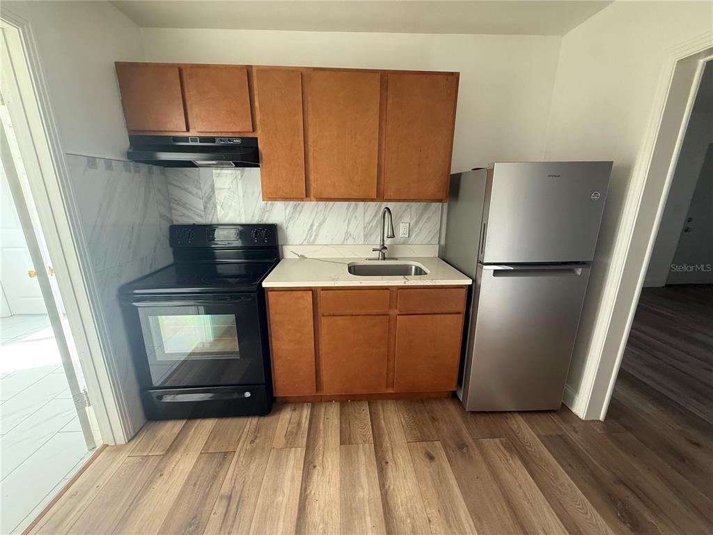 A small kitchen features wooden cabinets, a black stove, a stainless steel refrigerator, and marble-look backsplash — 6715 N ARMENIA AVENUE, TAMPA, FL
