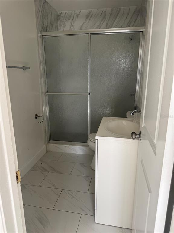 A small bathroom features a white vanity, a toilet, and a glass-enclosed shower stall — 6715 N ARMENIA AVENUE, TAMPA, FL