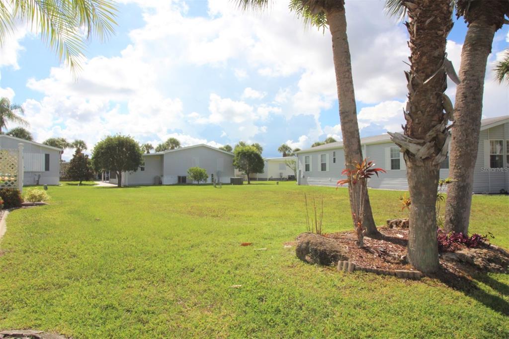 A grassy yard sits between several light-colored manufactured homes under a partly cloudy sky — 2100 KINGS HIGHWAY UNIT 145, PORT CHARLOTTE, FL