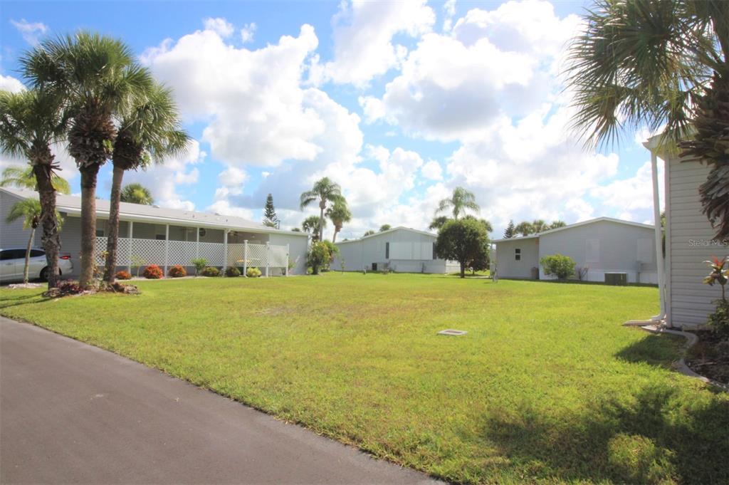A grassy yard sits between several manufactured homes under a blue sky with white clouds — 2100 KINGS HIGHWAY UNIT 145, PORT CHARLOTTE, FL