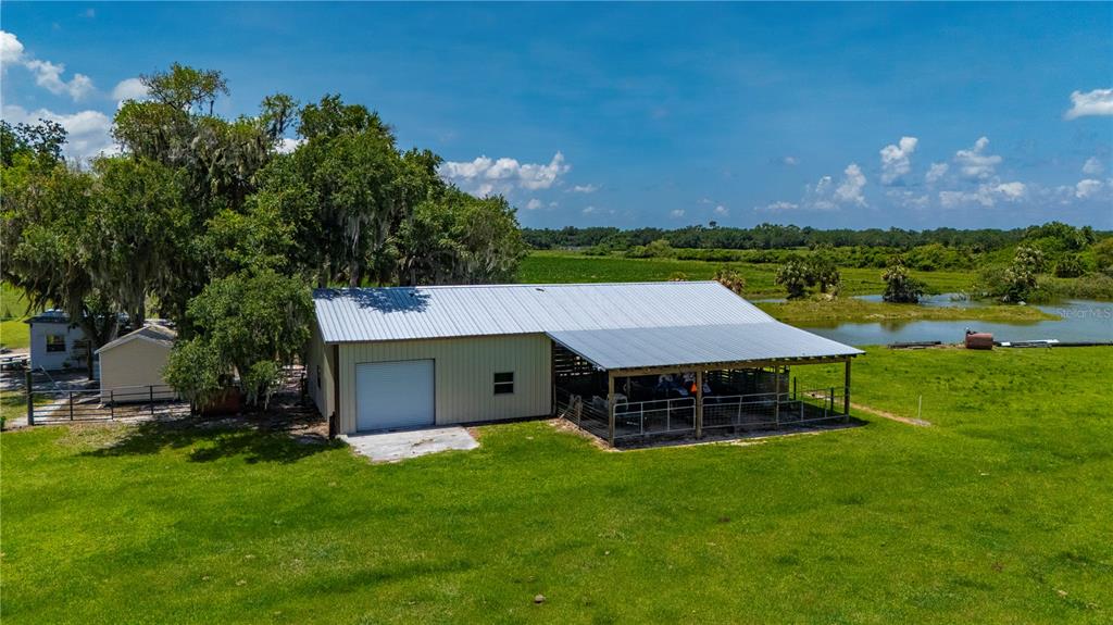 An aerial view shows a metal workshop with an attached carport on a grassy lot — 12241 SW GORDON HAY ROAD, ARCADIA, FL