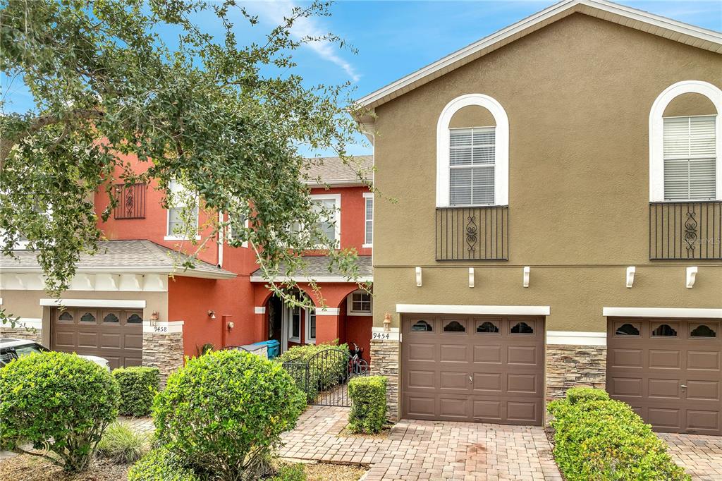 Two attached townhomes with brown garages, arched windows, and stone accents under a blue sky — 9454 SILVER BUTTONWOOD STREET, ORLANDO, FL