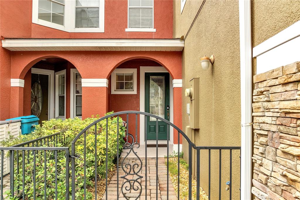 A gated entryway leads to a front door with a red stucco exterior and stone accents — 9454 SILVER BUTTONWOOD STREET, ORLANDO, FL