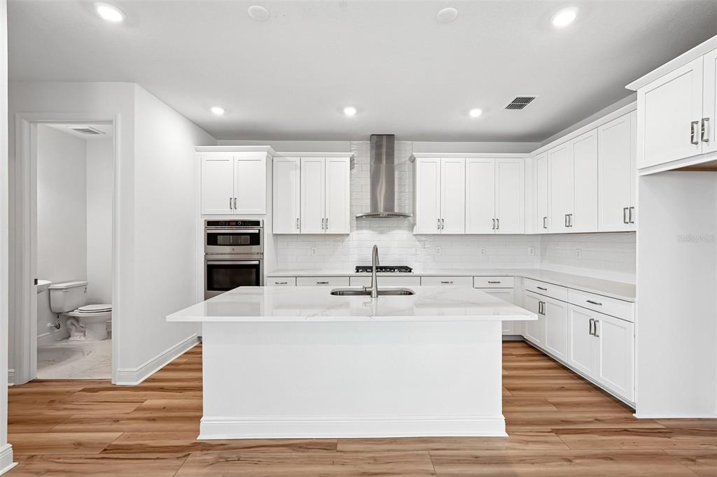 A modern white kitchen features a large center island, stainless steel appliances, and wood flooring — 8221 SEAFLOWER PARKWAY, BRADENTON, FL