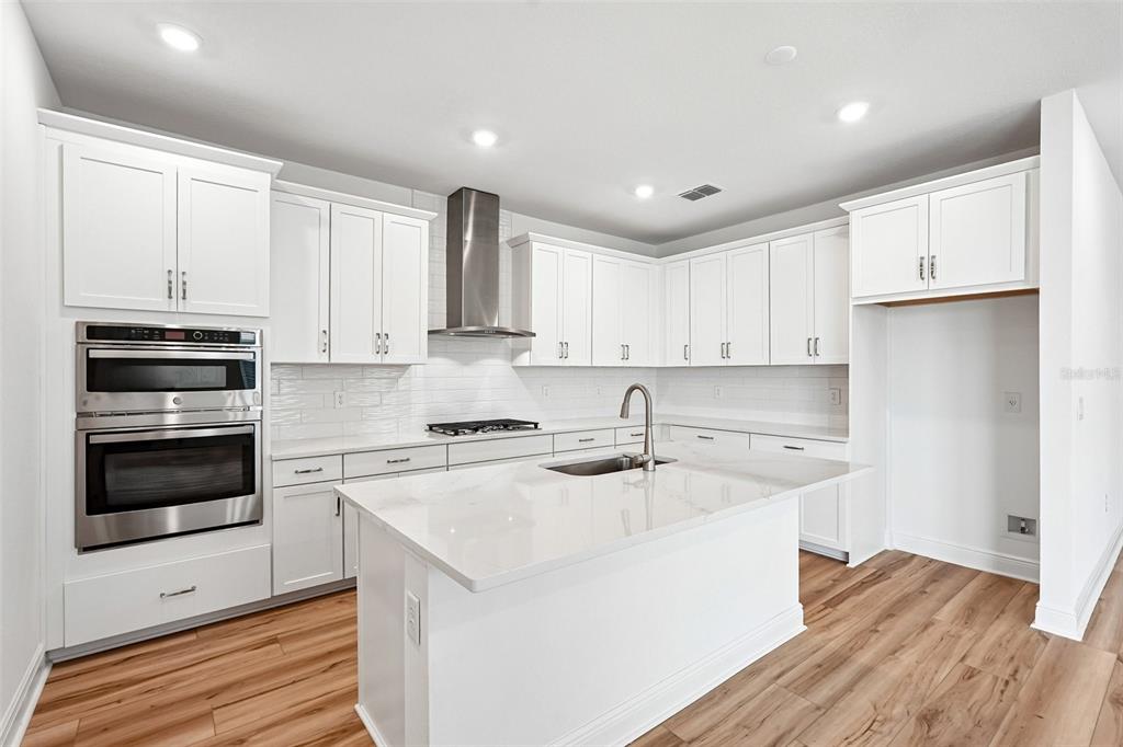 A modern kitchen features white cabinetry, stainless steel appliances, a center island, and wood flooring — 8221 SEAFLOWER PARKWAY, BRADENTON, FL