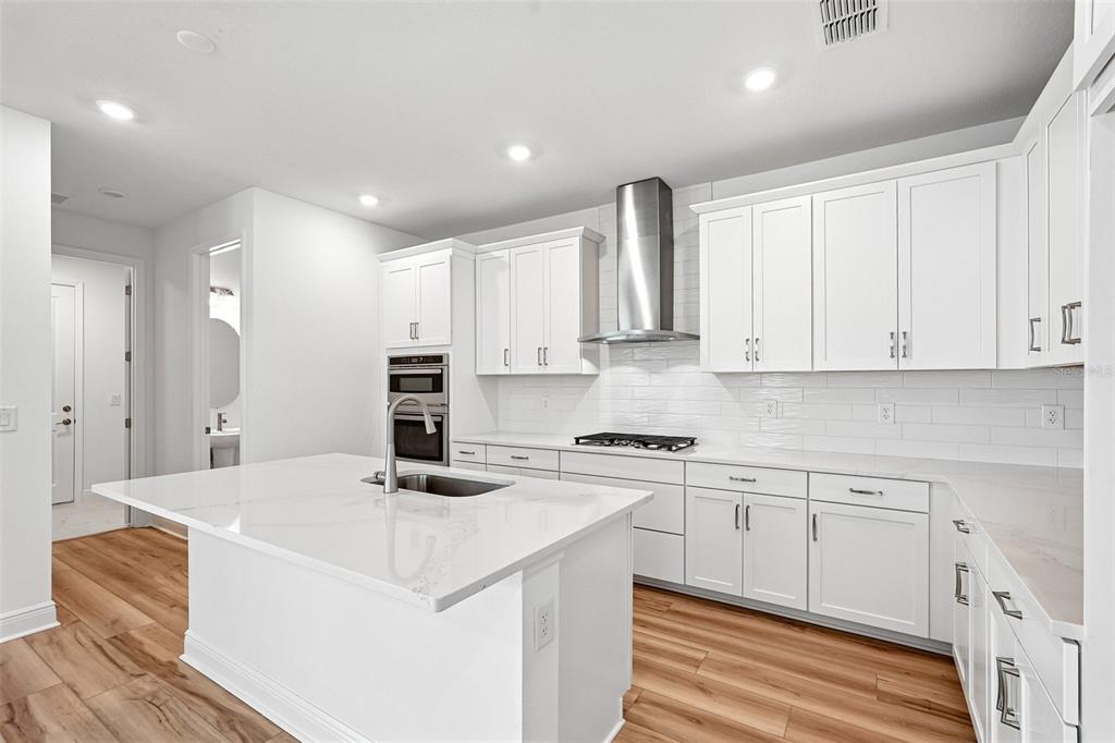 A modern kitchen features white cabinets, a large island with a sink, and wood flooring — 8221 SEAFLOWER PARKWAY, BRADENTON, FL