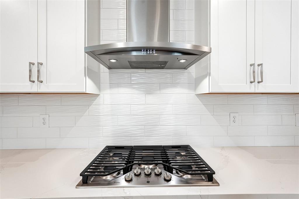 A stainless steel gas cooktop and range hood are centered between white kitchen cabinets — 8221 SEAFLOWER PARKWAY, BRADENTON, FL