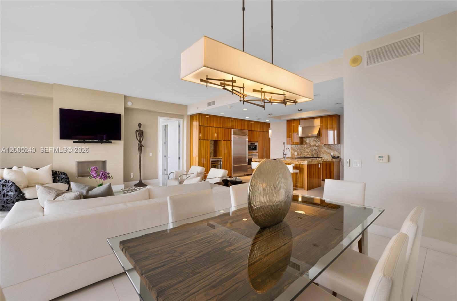 A modern open-concept living and dining area features wood cabinetry, white furniture, and a glass table — 9701 Collins Ave # 805S, Bal Harbour FL 33154, BAL HARBOUR, FL
