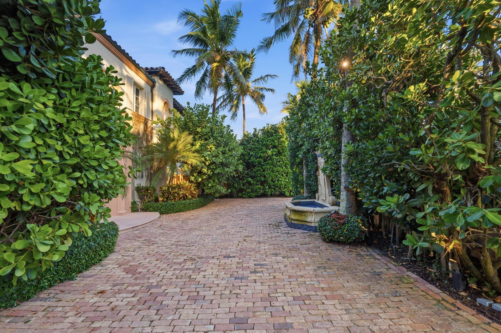 A brick driveway leads to a house entrance flanked by lush greenery and a stone fountain — 240 N Ocean Boulevard, Palm Beach FL 33480, PALM BEACH, FL
