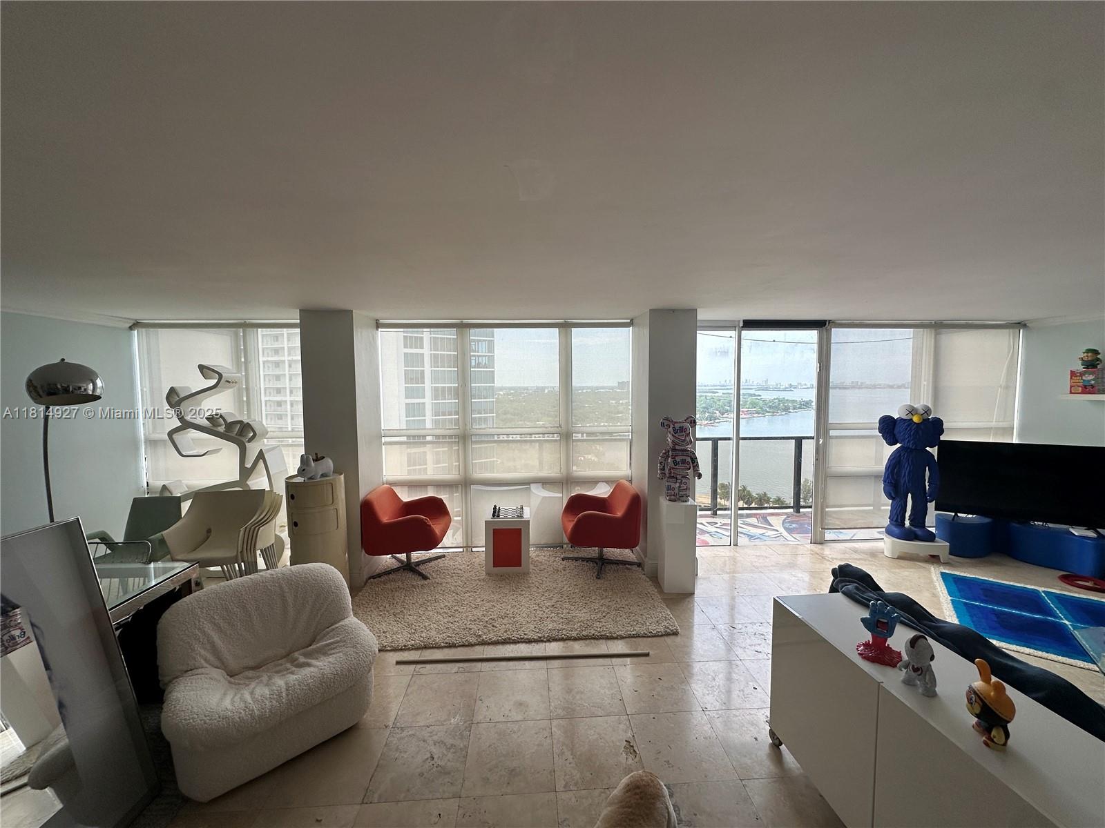 A bright living room features floor-to-ceiling windows with water views and modern art pieces — 600 NE 36th St, Miami FL 33137, MIAMI, FL