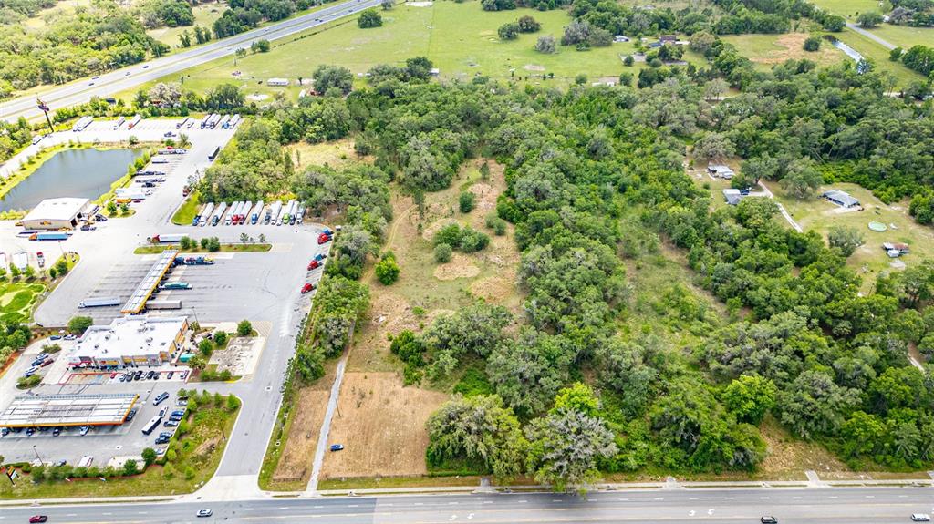 An aerial view shows a commercial parking lot adjacent to a large, wooded vacant lot — 2623 W C 48, BUSHNELL, FL