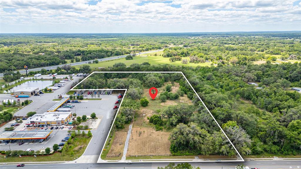 An aerial view shows a vacant, partially wooded lot adjacent to a commercial parking area — 2623 W C 48, BUSHNELL, FL