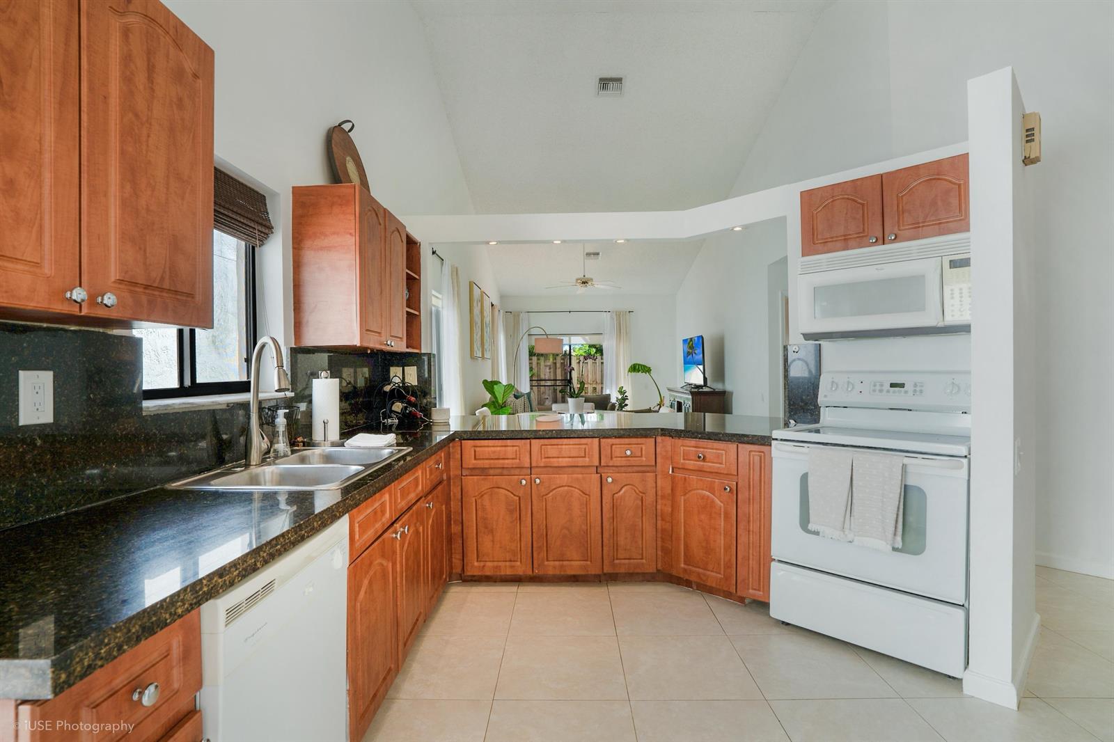 A kitchen with wood cabinets, dark granite countertops, and white appliances opens to a living area — 21712 Wapford Way, Boca Raton FL 33486, BOCA RATON, FL