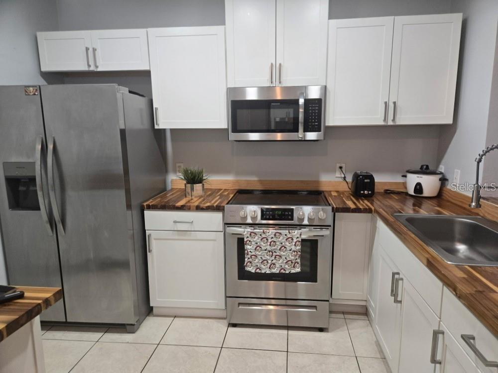A kitchen features white cabinets, stainless steel appliances, and wood-block countertops over tile flooring — 13226 GALICIA STREET UNIT 204, ORLANDO, FL