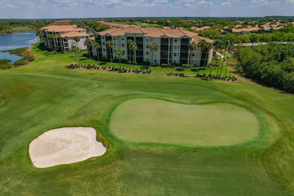An aerial view shows a golf course putting green with a sand bunker and apartment buildings — 7607 GRAND ESTUARY TRAIL UNIT 101, BRADENTON, FL