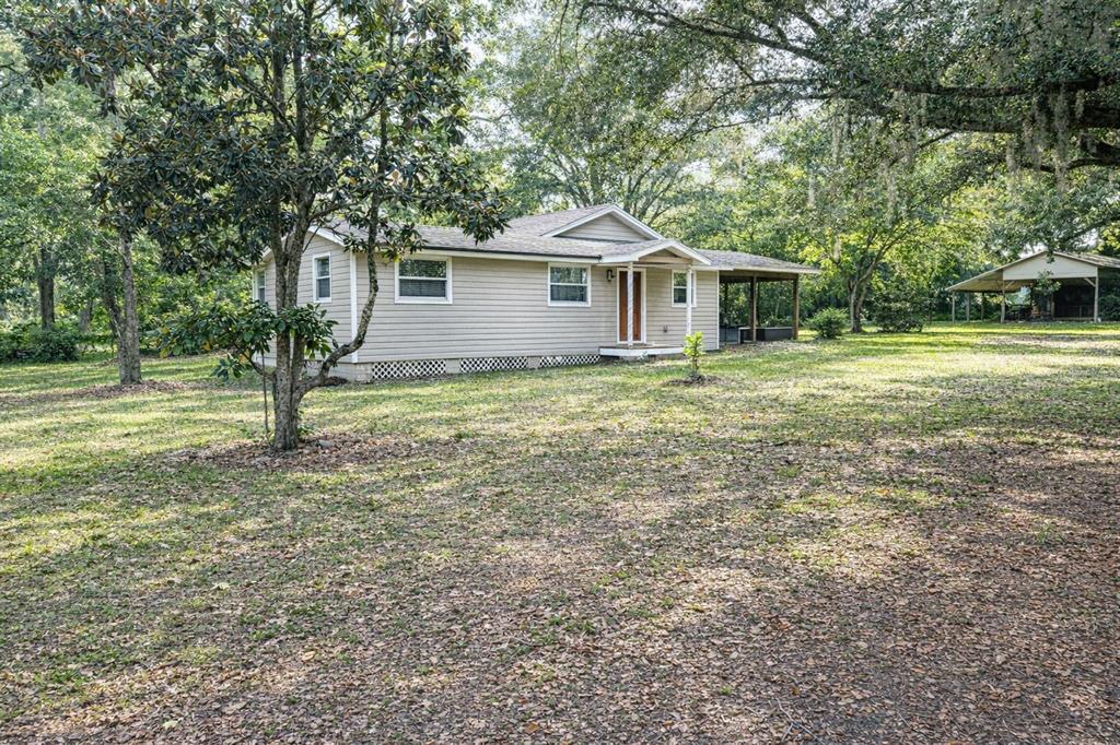 A single-story house with light siding and a covered porch sits on a wooded lot — 10019 CURLEY ROAD, SAN ANTONIO, FL