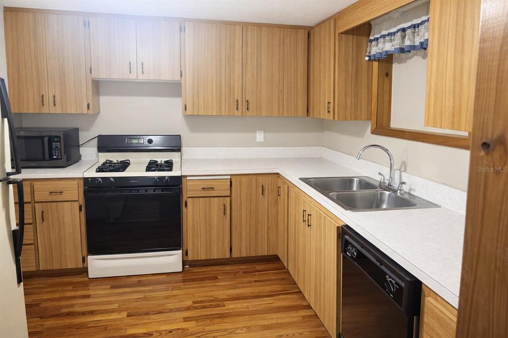 A kitchen features wood-grain cabinets, a black stove, a double sink, and hardwood flooring — 10019 CURLEY ROAD, SAN ANTONIO, FL