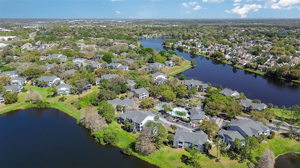 An aerial view shows a residential apartment complex situated along a winding lake — 717 SECRET HARBOR LANE UNIT 203, LAKE MARY, FL