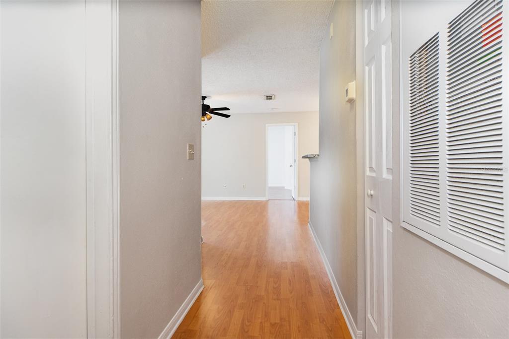 A hallway with light wood-look flooring leads to an open living area with a ceiling fan — 717 SECRET HARBOR LANE UNIT 203, LAKE MARY, FL