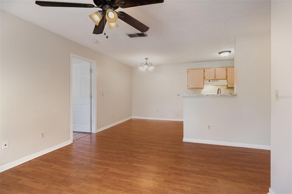 An open-concept dining area with wood-look flooring leads to a kitchen with light wood cabinets — 717 SECRET HARBOR LANE UNIT 203, LAKE MARY, FL