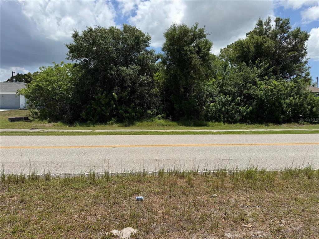 A vacant, tree-covered residential lot sits across a paved road from a suburban house — 9798 GULFSTREAM BOULEVARD, ENGLEWOOD, FL