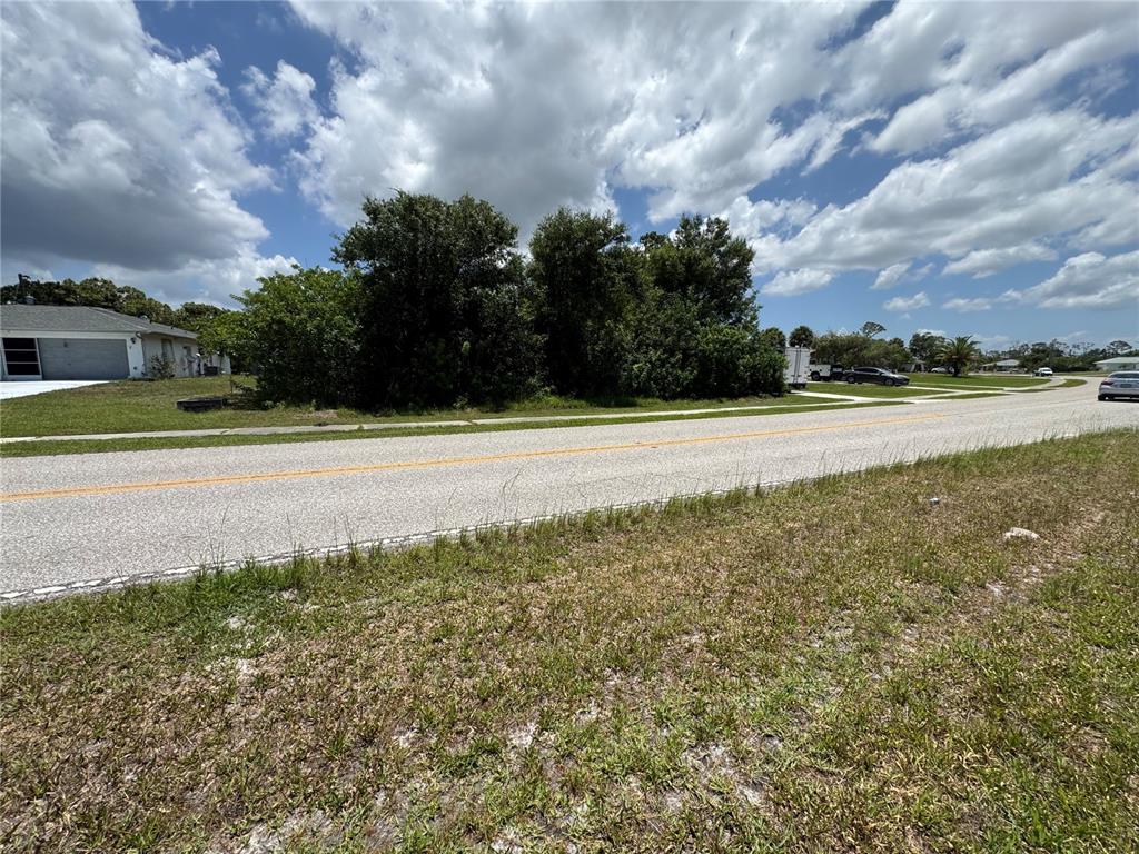 A vacant, tree-covered residential lot sits beside a paved road under a cloudy sky — 9798 GULFSTREAM BOULEVARD, ENGLEWOOD, FL
