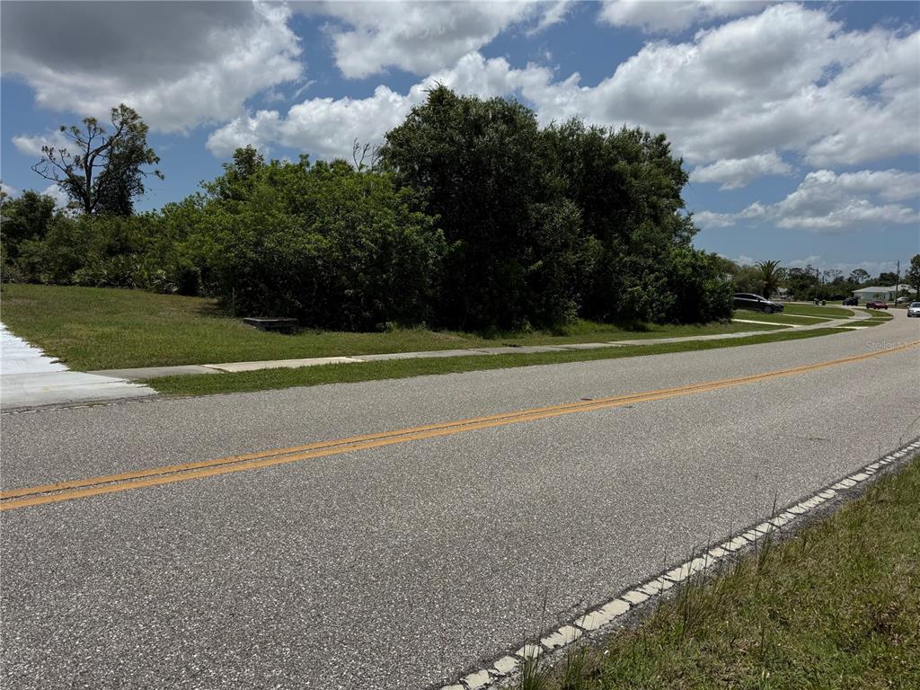 A vacant, tree-covered lot sits adjacent to a paved road under a cloudy sky — 9798 GULFSTREAM BOULEVARD, ENGLEWOOD, FL