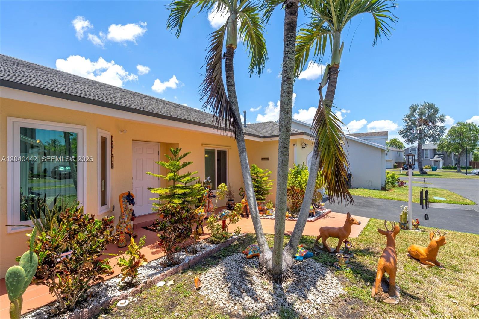 The exterior of a yellow house features a front porch with palm trees and statues — 10170 NW 54th Ter, Doral FL 33178, DORAL, FL