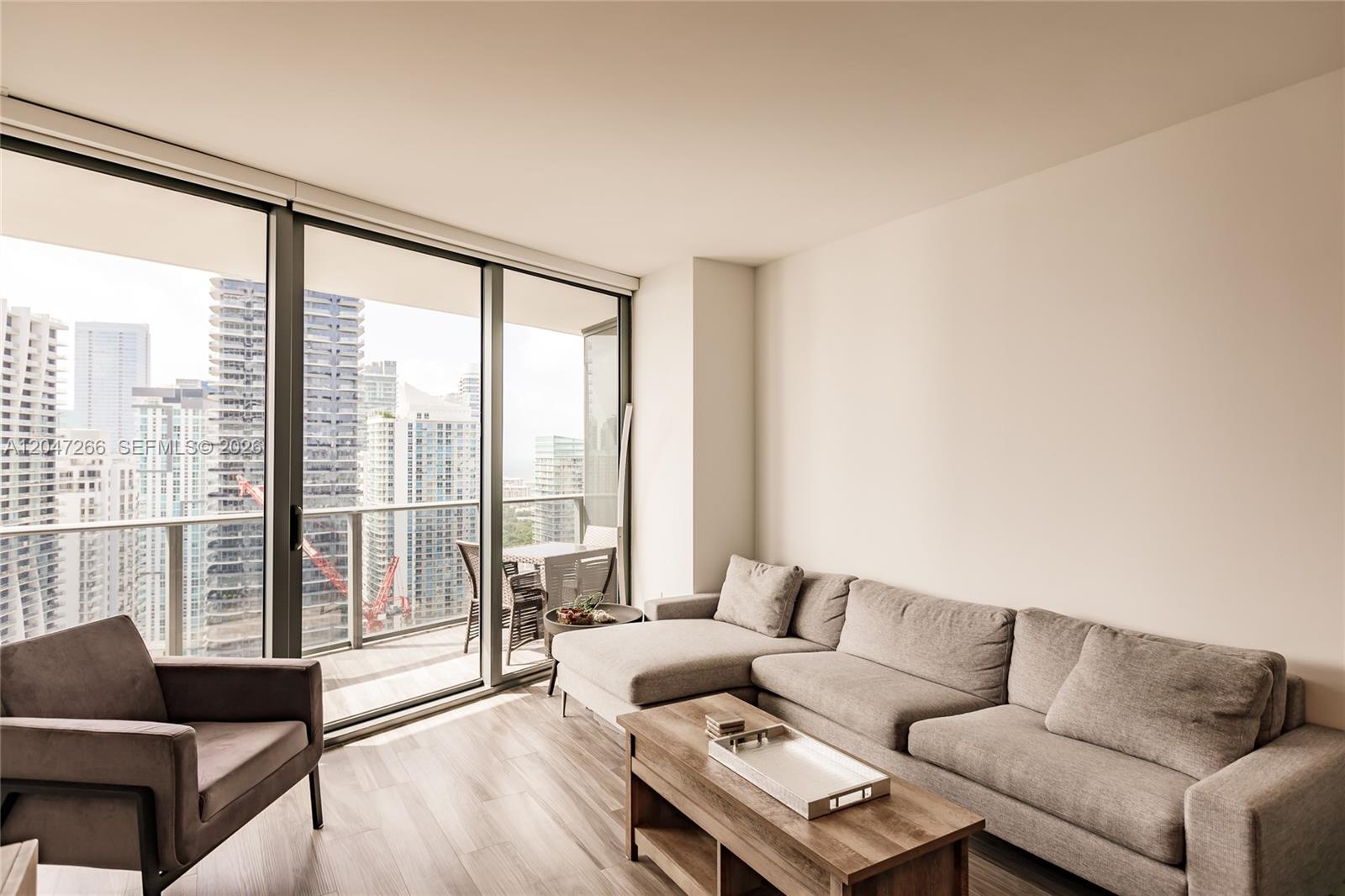 A living room features a gray sectional sofa, a wooden coffee table, and floor-to-ceiling windows — 801 S Miami Ave # 3703, Miami FL 33130, MIAMI, FL