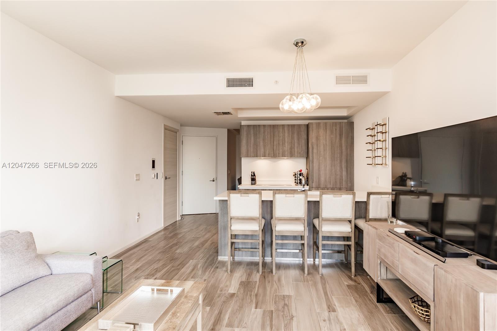 A modern living room and kitchen area features wood-look flooring, bar seating, and neutral decor — 801 S Miami Ave # 3703, Miami FL 33130, MIAMI, FL