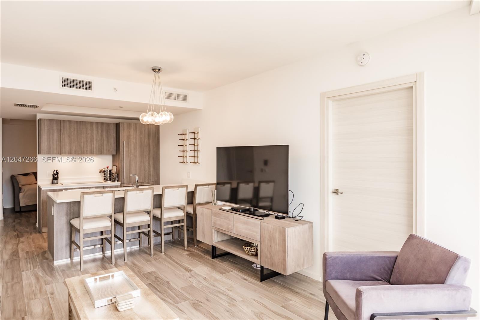 A modern living room and kitchen area features wood-look flooring, light cabinetry, and a television — 801 S Miami Ave # 3703, Miami FL 33130, MIAMI, FL