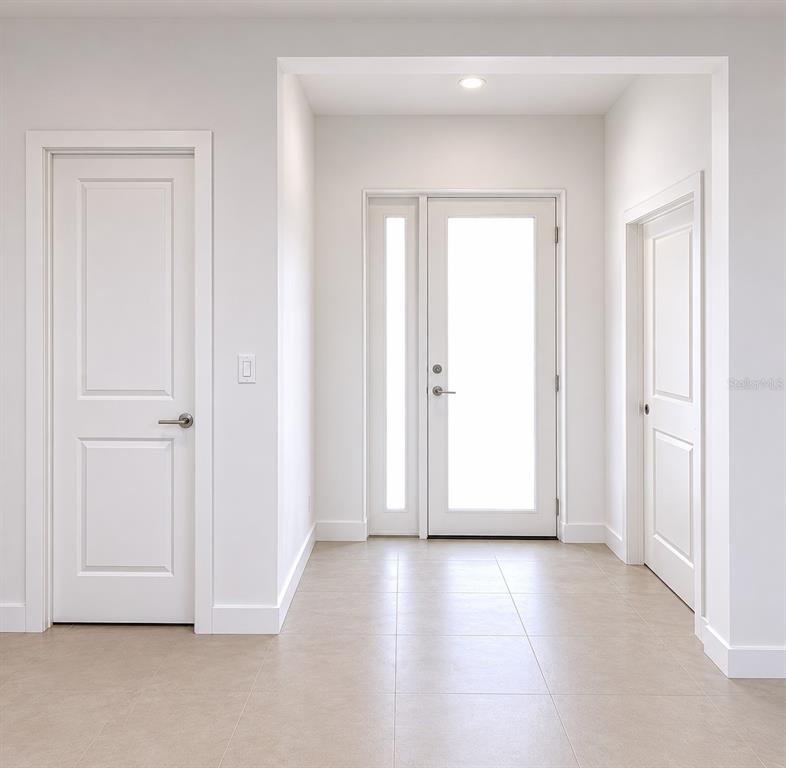 A bright entryway features a white front door with a sidelight, tiled flooring, and two interior doors — 503 10 STREET W, LEHIGH ACRES, FL