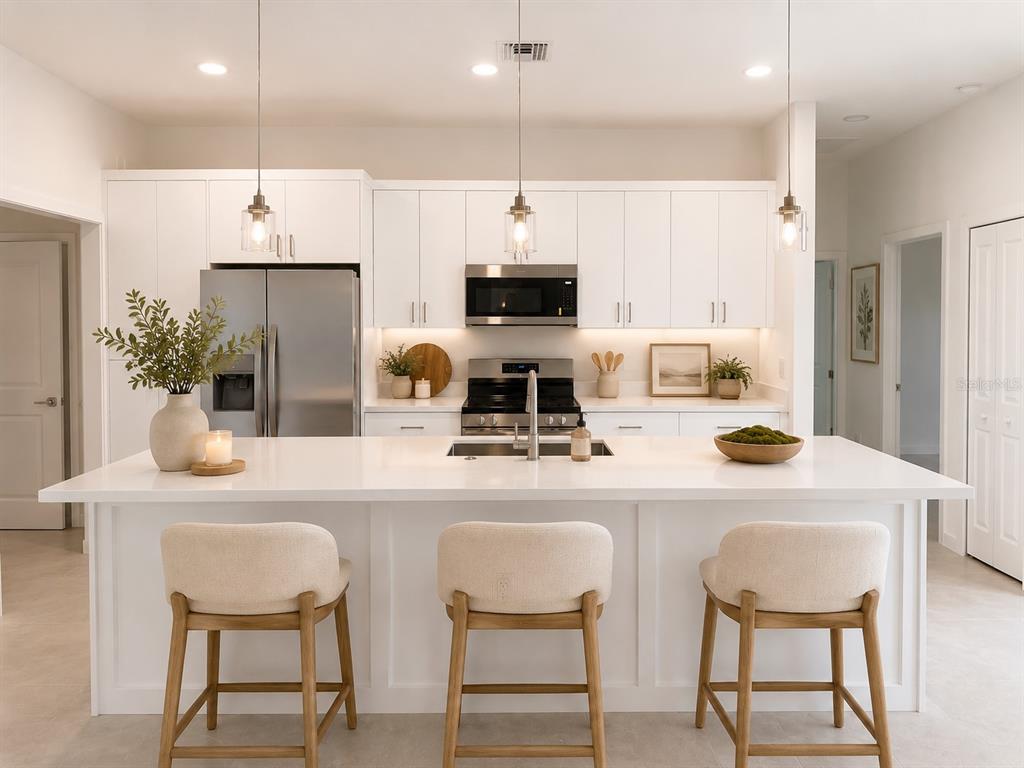 A modern kitchen features white cabinetry, a large quartz island, and three upholstered bar stools — 503 10 STREET W, LEHIGH ACRES, FL