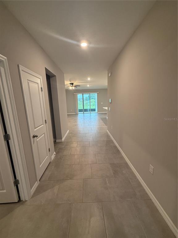A hallway with light gray tile flooring leads toward a living area with sliding glass doors — 32434 OSPREY PEAK WAY, SAN ANTONIO, FL