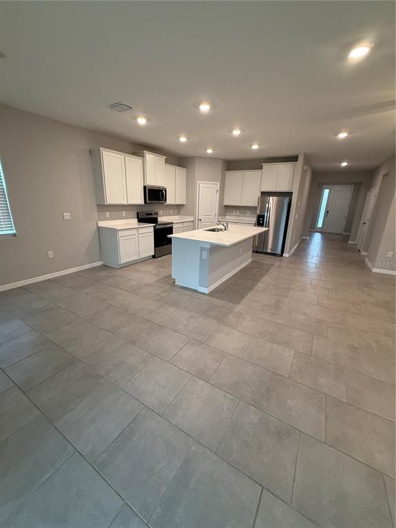 A modern kitchen features white cabinets, stainless steel appliances, a center island, and tile flooring — 32434 OSPREY PEAK WAY, SAN ANTONIO, FL