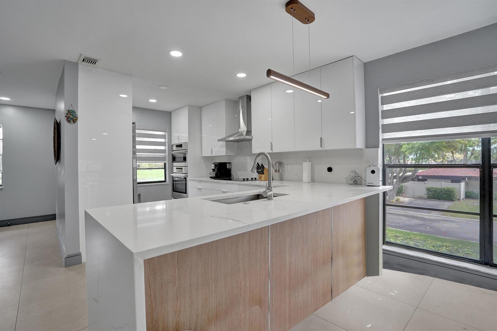 A modern kitchen features white cabinets, a light wood-paneled island, and a large window — 21675 Tall Palm Circle # 2b, Boca Raton FL 33433, BOCA RATON, FL