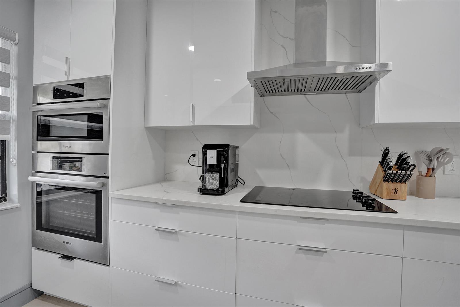 A modern kitchen features white cabinets, stainless steel appliances, and a marble-patterned backsplash — 21675 Tall Palm Circle # 2b, Boca Raton FL 33433, BOCA RATON, FL