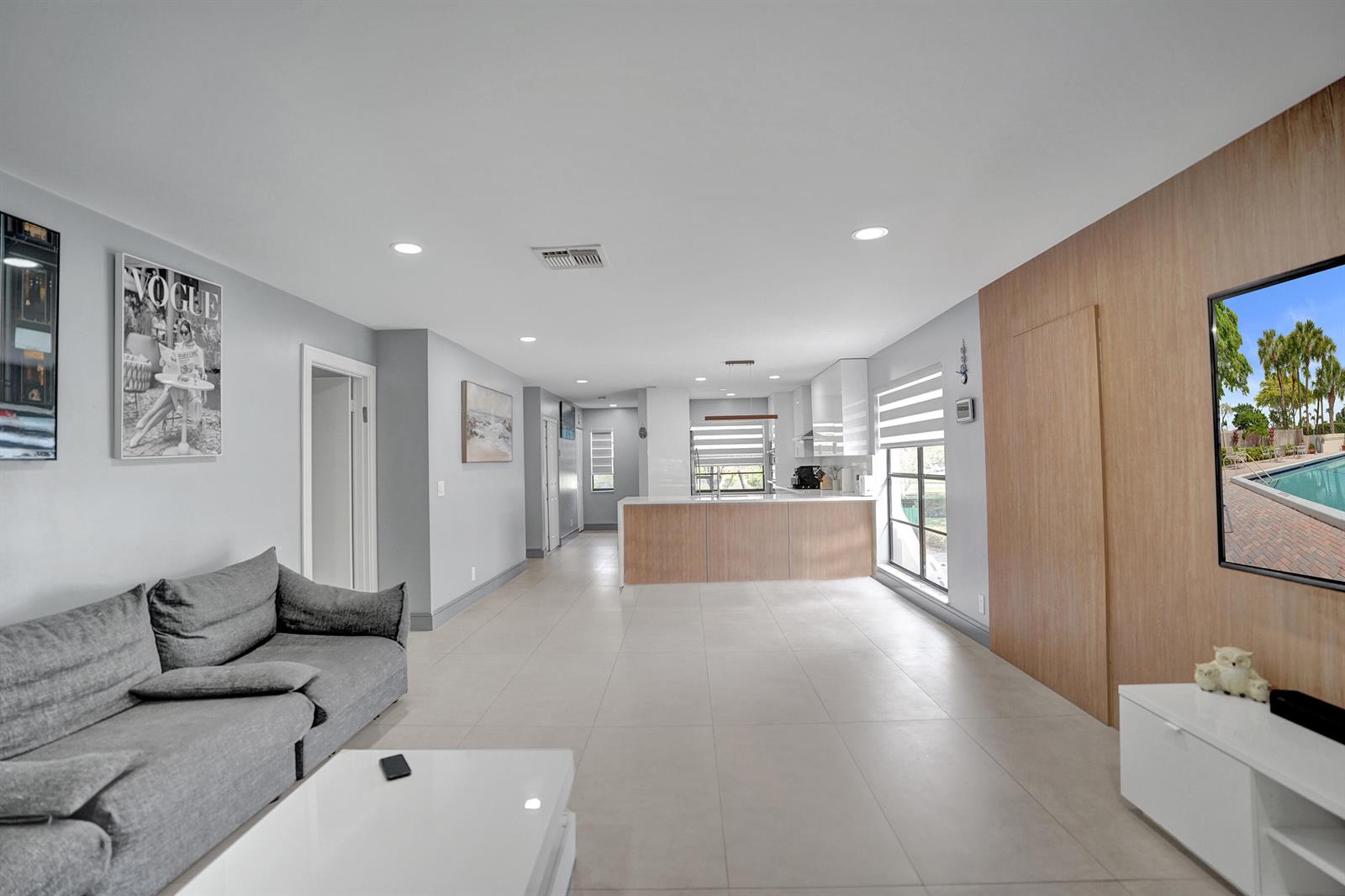 A modern open-concept living room and kitchen featuring light tile floors and wood paneling — 21675 Tall Palm Circle # 2b, Boca Raton FL 33433, BOCA RATON, FL
