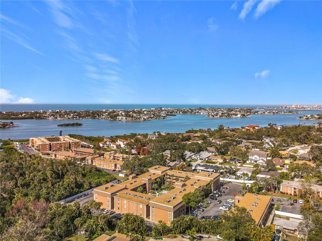 An aerial view shows multi-story apartment buildings surrounded by trees near a coastal waterway — 12760 INDIAN ROCKS ROAD UNIT 583, LARGO, FL