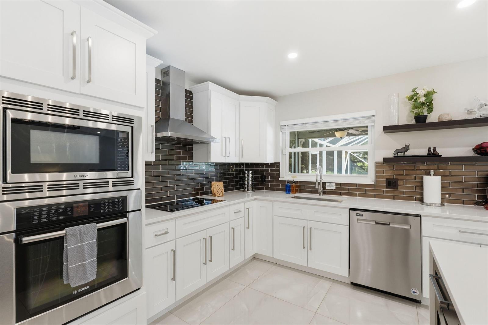 A modern kitchen features white cabinets, stainless steel appliances, and dark brown subway tile backsplashes — 1799 Shower Tree Way, Wellington FL 33414, WELLINGTON, FL