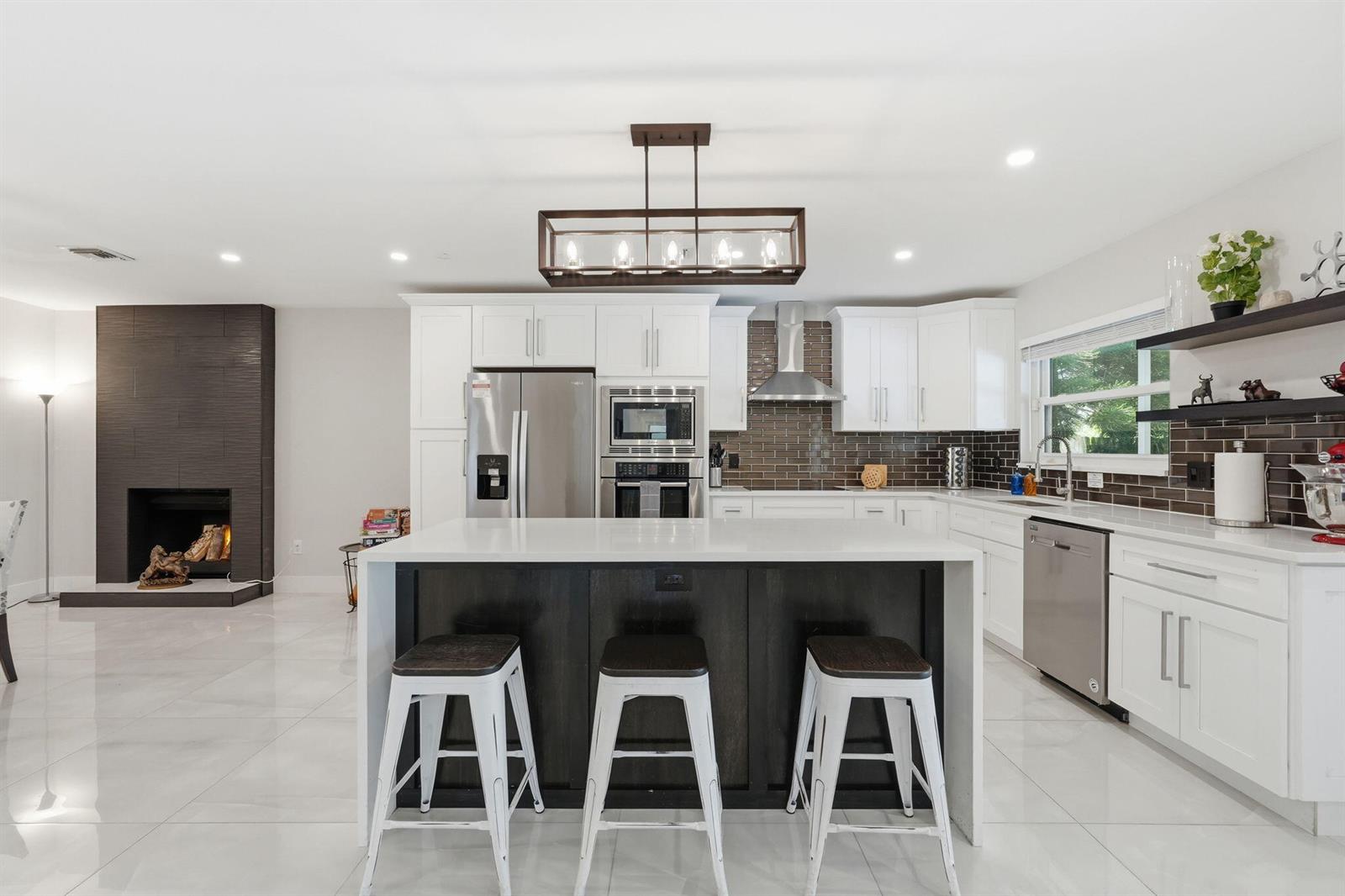 A modern kitchen features white cabinets, a dark wood island with stools, and a fireplace — 1799 Shower Tree Way, Wellington FL 33414, WELLINGTON, FL