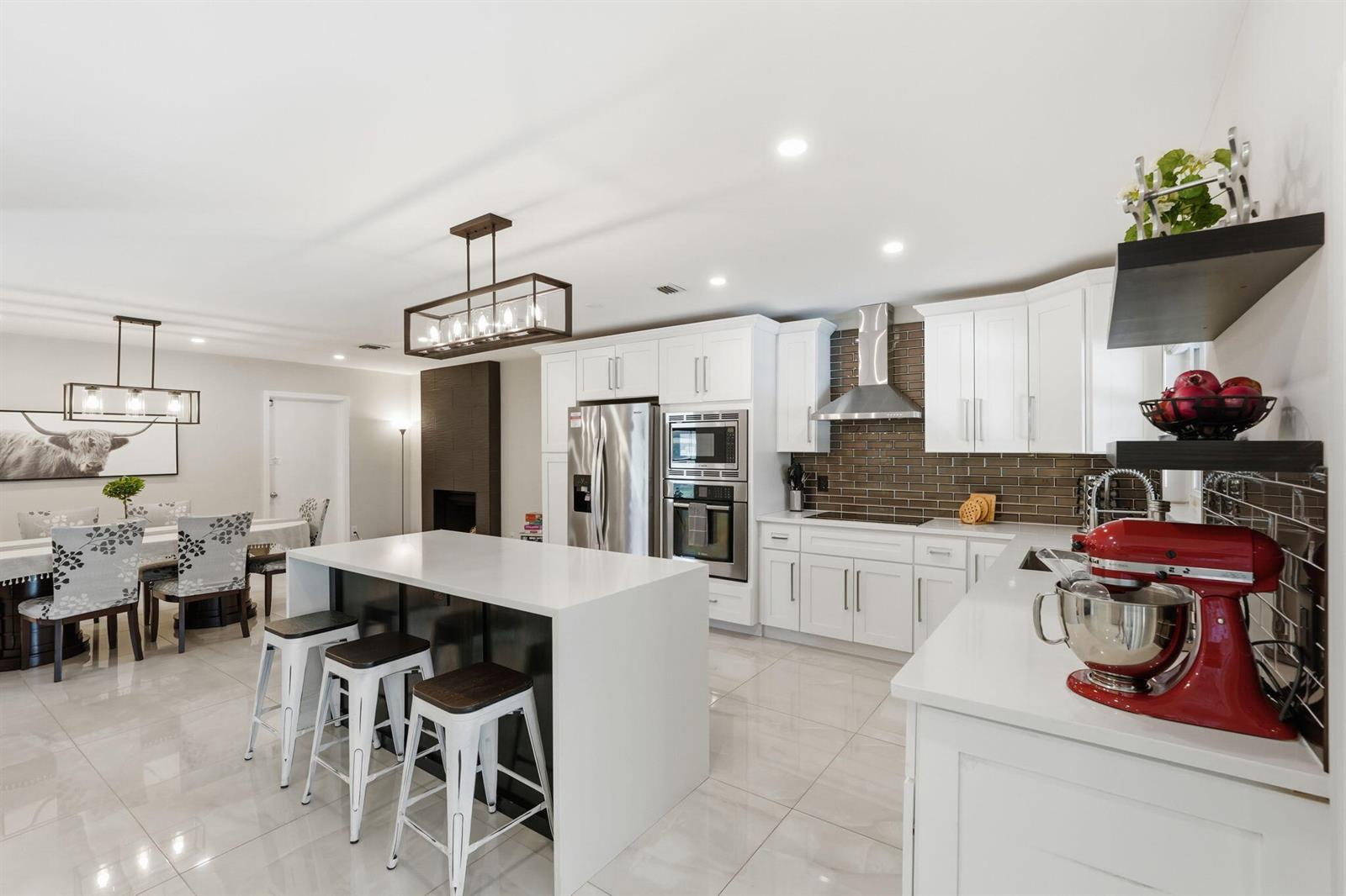 A modern kitchen features white cabinets, a central island with bar stools, and tiled floors — 1799 Shower Tree Way, Wellington FL 33414, WELLINGTON, FL
