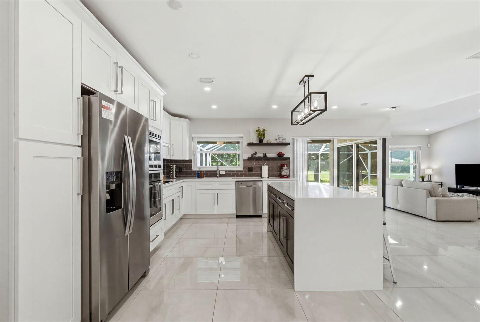 A modern kitchen features white cabinetry, stainless steel appliances, a dark island, and tile flooring — 1799 Shower Tree Way, Wellington FL 33414, WELLINGTON, FL