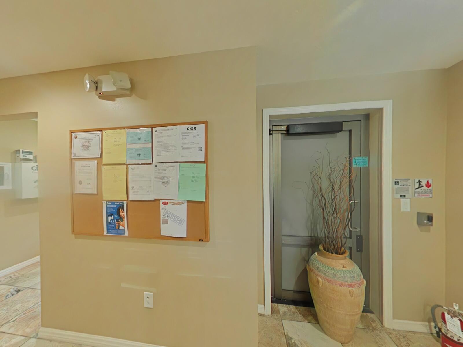 A beige hallway features a bulletin board, a decorative floor vase, and a metal door — 806 NW 9th Street, Okeechobee FL 34972, OKEECHOBEE, FL