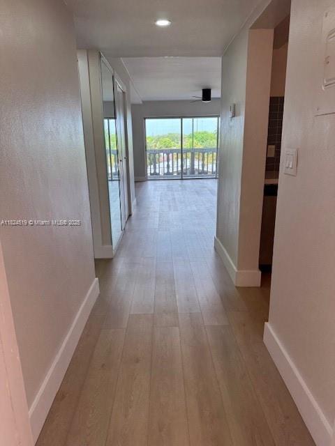 A hallway with light wood-look flooring leads toward a living area with a balcony view — 215 SE 3rd Ave # 307B, Hallandale Beach FL 33009, HALLANDALE BEACH, FL