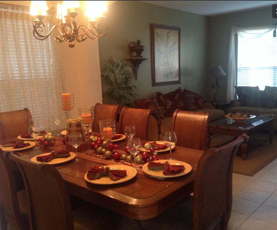 A dining room with a wooden table set for dinner, adjacent to a living area — 8646 LA ISLA DRIVE, KISSIMMEE, FL