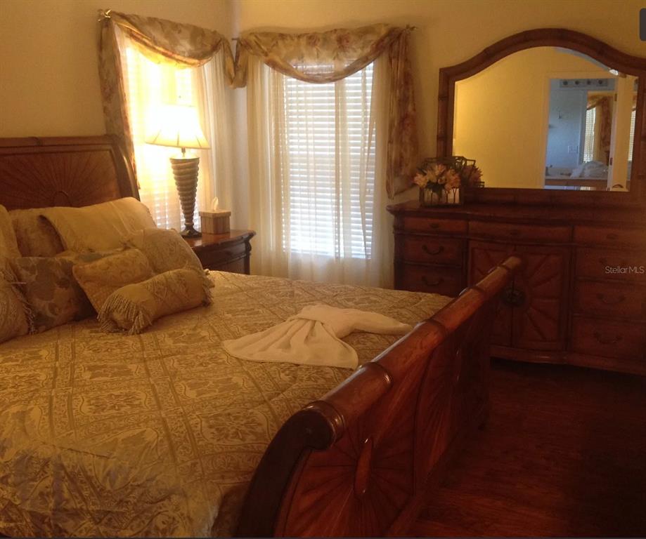 A bedroom features a wooden bed frame, a matching dresser with a mirror, and window curtains — 8646 LA ISLA DRIVE, KISSIMMEE, FL