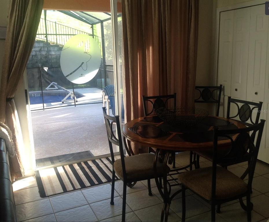 A dining area with a round table and chairs overlooks a screened-in pool patio — 8646 LA ISLA DRIVE, KISSIMMEE, FL